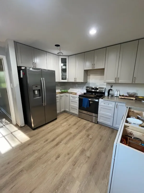 Kitchen remodel with gray shaker cabinets, stainless refrigerator, and light wood flooring