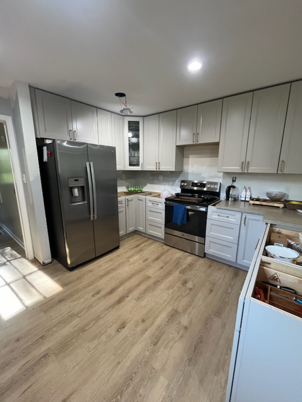 Kitchen remodel with gray shaker cabinets, stainless refrigerator, and light wood flooring