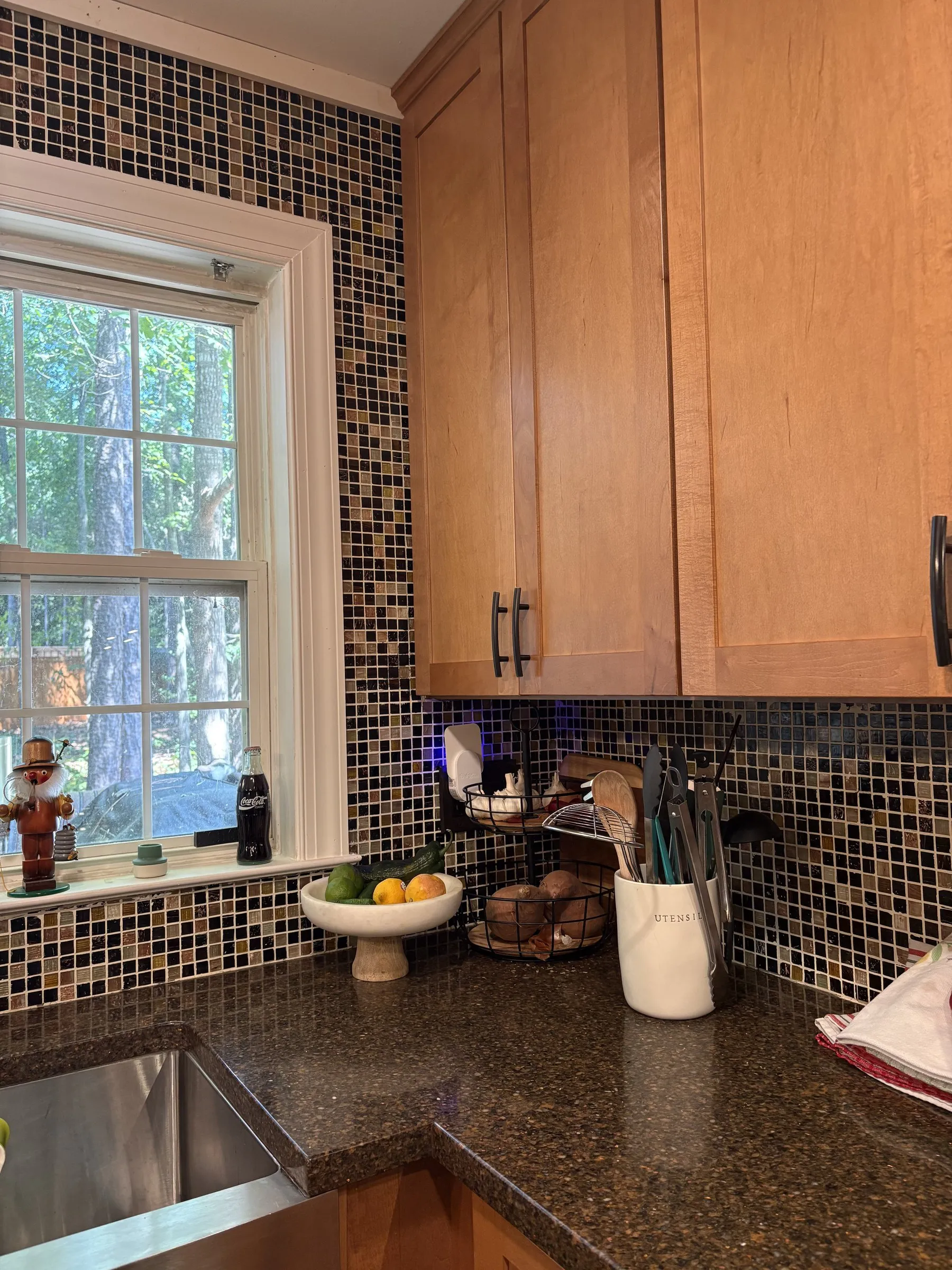 Kitchen window and wood cabinets framed by a mosaic tile backsplash